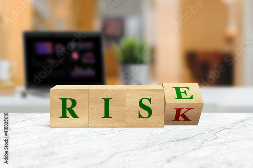 Wooden block flip over block RISK to RISE word on table background.