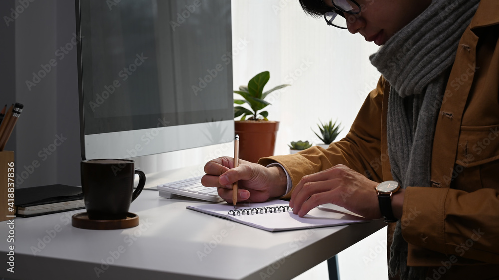 Cropped shot of young man designer sitting at modern workplace and making note on notebook. Cropped shot of young man designer sitting at modern workplace and making note on notebook.
