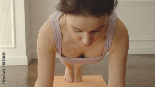 Young adult woman standing in the plank position on a yoga mat at home photo