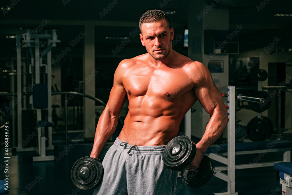 Naklejka premium Bodybuilder training with dumbbells. Sportsman with naked torso. Sporty workout. Athletic body.