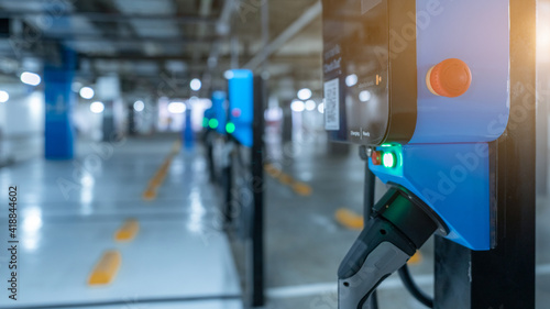 Blurred electric car charging station for charge EV battery. Plug for vehicle with electric engine. EV charger. Clean energy. Charging point at car parking lot. Future transport technology.