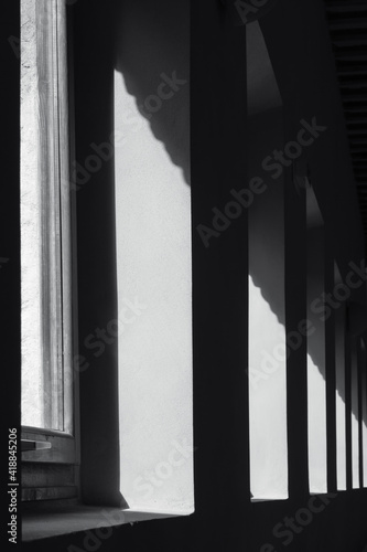 Detail of the geometry of a corridor with light entering through the windows and the shadow of the interior. Monochrome. Vertical view.