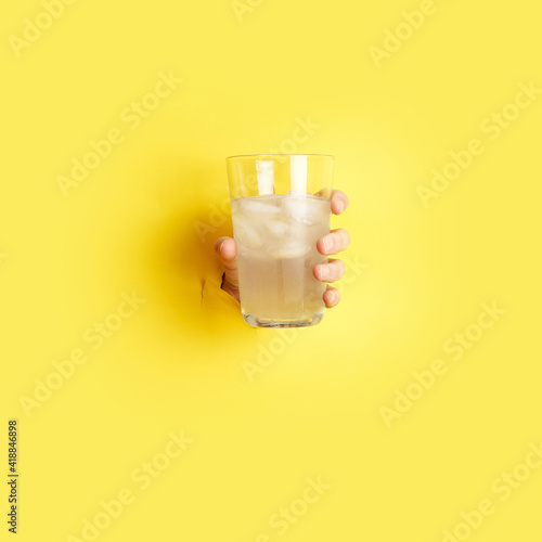 woman hand holding glass with lemonade through the hole in yellow paper . High quality photo