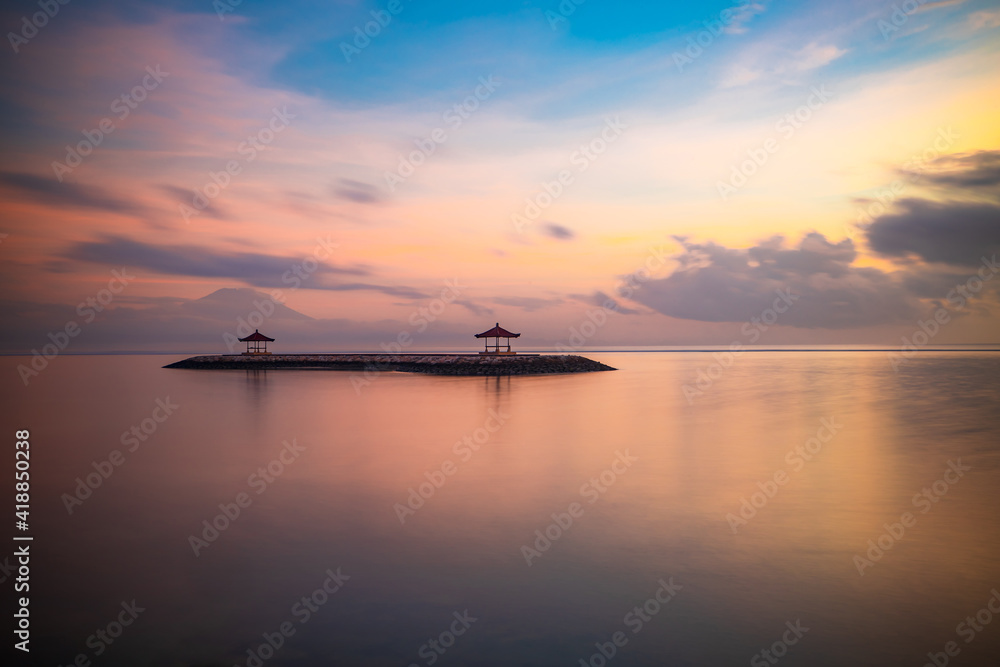Pink sunrise. Seascape background. Traditional gazebos on an artificial island in the ocean. Water reflection. Calm water surface. Soft focus. Copy space. Sanur beach, Bali.