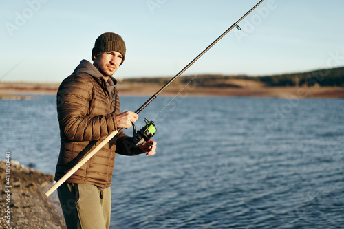 Young fisherman standing on the shore of lake with fishing rod