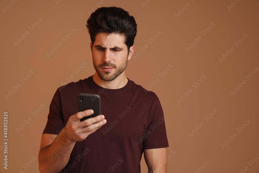 Focused masculine man using mobile phone while posing on camera Focused masculine man using mobile phone while posing on camera