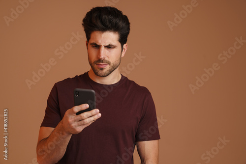Focused masculine man using mobile phone while posing on camera