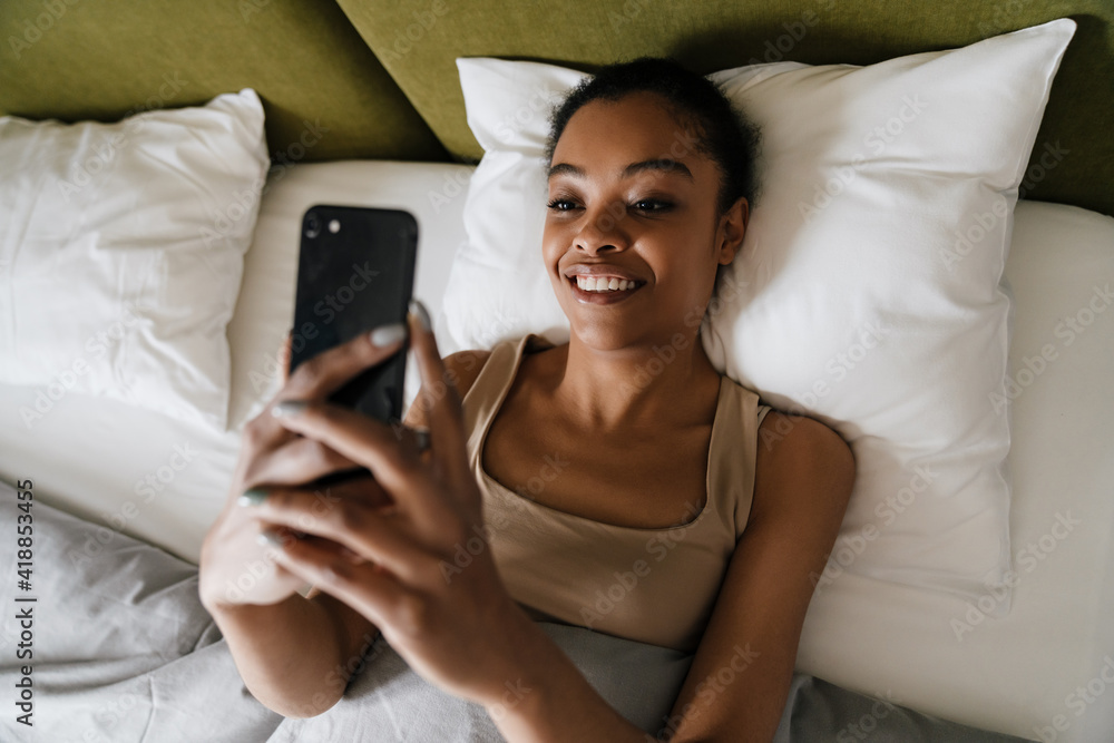 Happy african american girl using mobile phone while lying in bed Happy african american girl using mobile phone while lying in bed