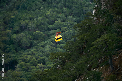 cabin of the aerial tram moves over wooded mountain slopes