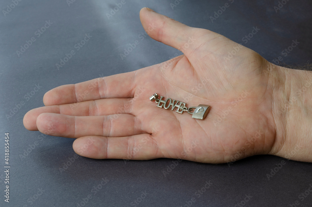 Silver word love with a padlock in an open male palm on a gray background. Silver word love with a padlock in an open male palm on a gray background.