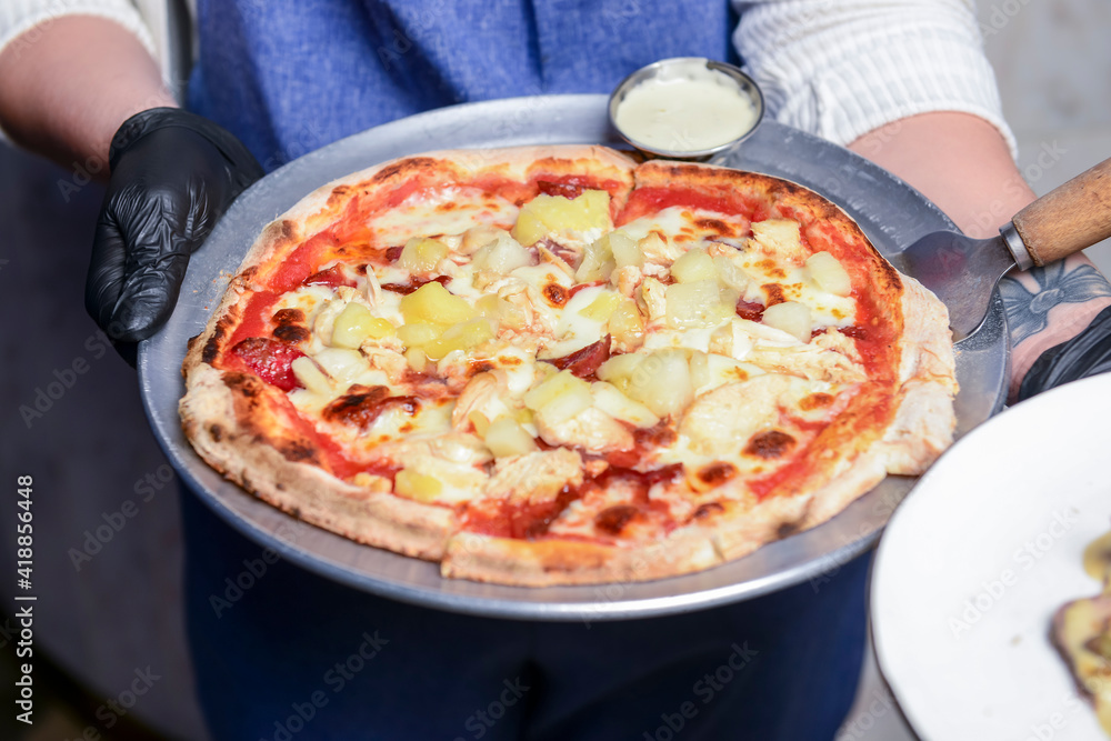 Gourmet pizza with barbeque sauce, grilled chicken, cheese served by waiter in restaurant or diner.