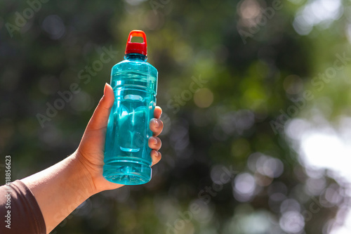 Clear blue green water bottle, the lid is red with a hole in the center for portability, natural background. With the hand held Drinking with vitamins Drink water in summer Leave space for the text.