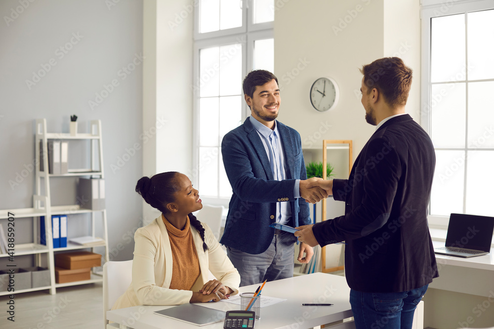 Obraz premium Caucasian man and his African-American wife receive greetings from a financial advisor with a rental home and a mortgage. Bank manager shakes hands with happy customers in the office at a meeting.