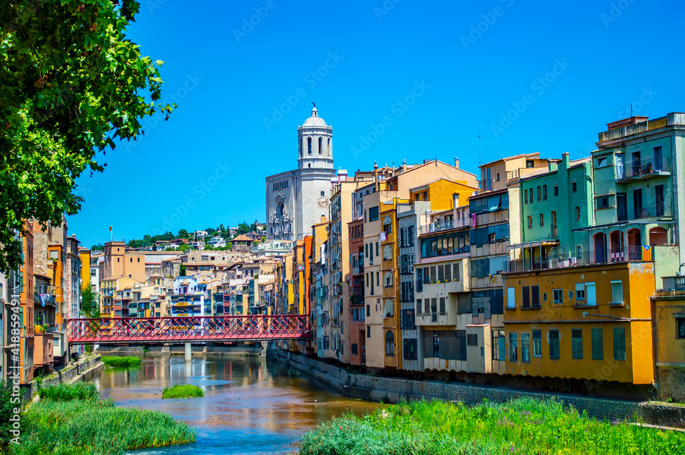 Girona, Spain - July 28, 2019: Colorful houses of the Jewish quarter of Girona with Eiffel Bridge and Saint Mary cathedral in the backgroun