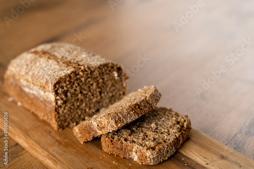 Close up of a loaf of bread that has been sliced sitting on a wooden table.  Whole wheat and whole grain bread.