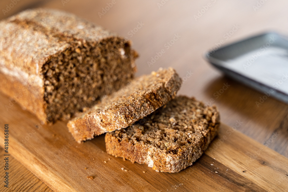 Close up of a loaf of bread that has been sliced sitting on a wooden table.  Whole wheat and whole grain bread.