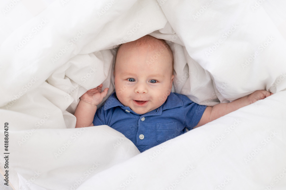smiling baby boy in a blanket in a crib, happy newborn woke up in the morning or goes to bed