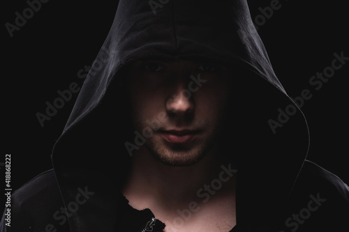 Silhouette of a man in a hood or a bully on a black background. The face of a man of a lawbreaker in the twilight