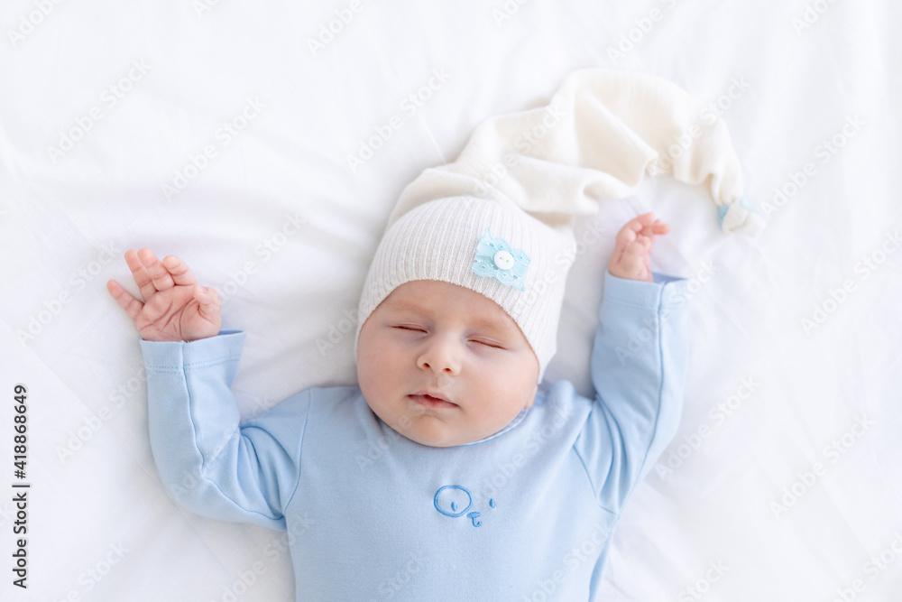 baby boy sleeps on the bed lying on his back in blue pajamas with his hands up, healthy newborn sleep baby boy sleeps on the bed lying on his back in blue pajamas with his hands up, healthy newborn sleep