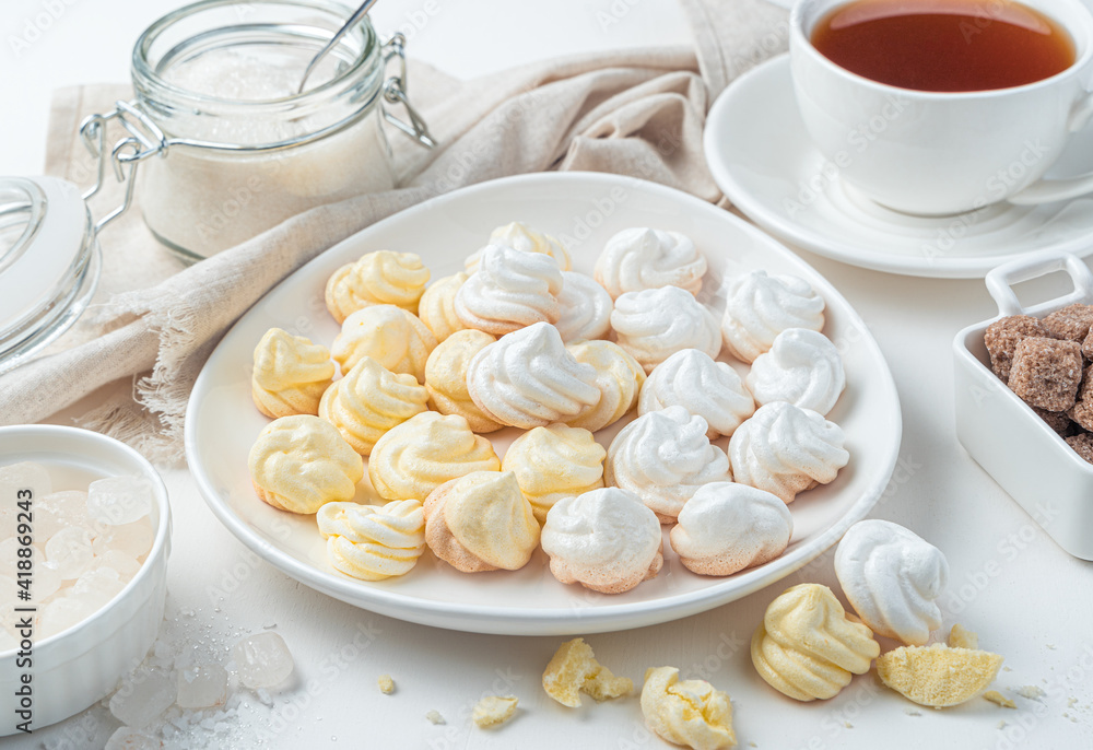Still life with Swiss meringues on, tea, napkin and sugar on a light background. Side view. Still life with Swiss meringues on, tea, napkin and sugar on a light background. Side view.