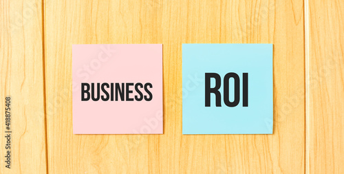 Inscription BusiNESS ROI on pink and blue square sticky sticker on wooden wall