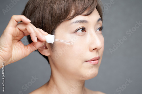 顔に美容液を垂らす中年の日本人女性