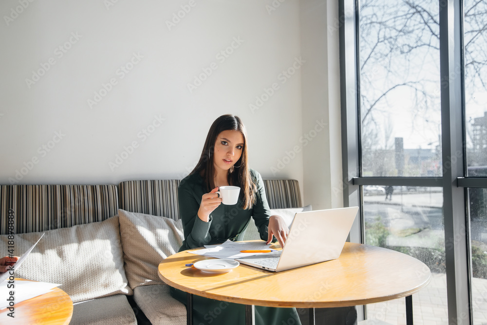 A young beautiful girl is sitting in a cafe, working at a computer and communicating in social networks. A young beautiful girl is sitting in a cafe, working at a computer and communicating in social networks.