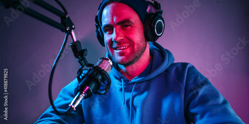 Portrait of streamer broadcasting his audio show at home studio using stylish cyber punk blue magenta ambient light