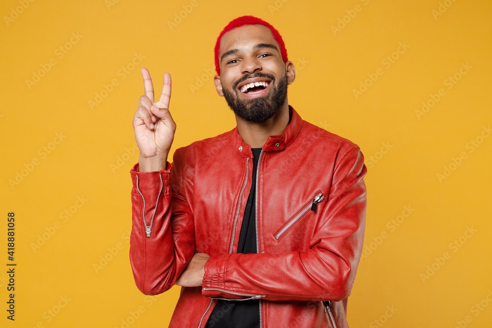 Young african dark-skinned happy smiling man 20s with funky trendy pink hairdo wear stylish red leather jacket show victory v-sign gesture isolated on yellow orange color background studio portrait Young african dark-skinned happy smiling man 20s with funky trendy pink hairdo wear stylish red leather jacket show victory v-sign gesture isolated on yellow orange color background studio portrait