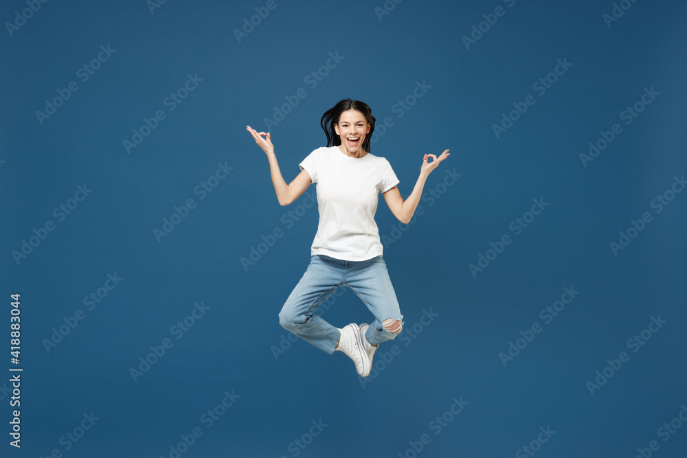 Full length young brunette latin woman 20s in white casual basic t-shirt hold hands in yoga gesture, relax meditating, try to calm down jumping high isolated on dark blue background studio portrait. Full length young brunette latin woman 20s in white casual basic t-shirt hold hands in yoga gesture, relax meditating, try to calm down jumping high isolated on dark blue background studio portrait.