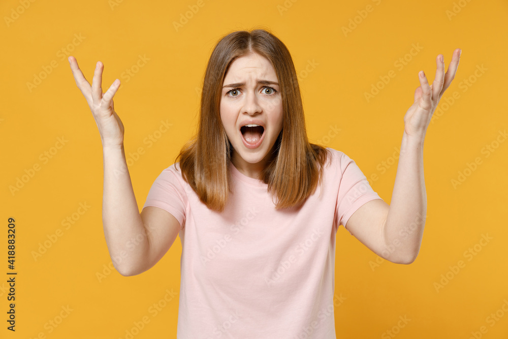 Young indignant shocked expressive angry woman 20s in casual basic pastel pink t-shirt, blank print design look camera spread hand shouting scream isolated on yellow color background studio portrait Young indignant shocked expressive angry woman 20s in casual basic pastel pink t-shirt, blank print design look camera spread hand shouting scream isolated on yellow color background studio portrait