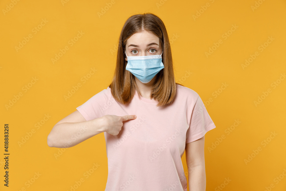 Young surprised woman 20s wearing basic pastel pink t-shirt in sterile face mask coronavirus covid-19 pandemic quarantine point index finger on herself isolated on yellow background studio portrait Young surprised woman 20s wearing basic pastel pink t-shirt in sterile face mask coronavirus covid-19 pandemic quarantine point index finger on herself isolated on yellow background studio portrait