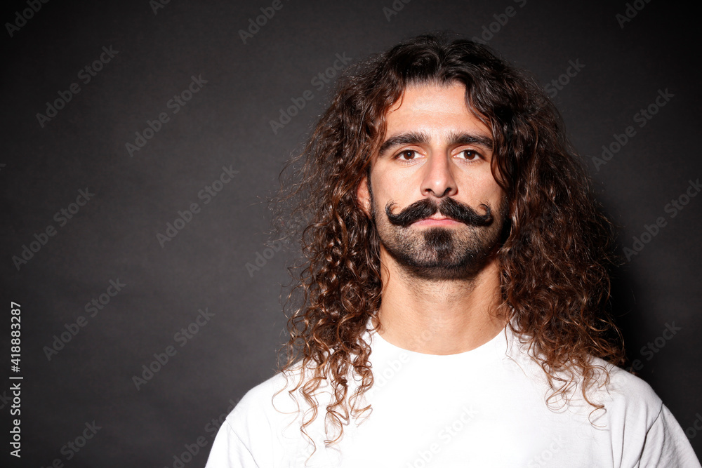 Uomo con baffi a "manubrio" e capelli lunghi guarda con aria seria ,  isolato su sfondo scuro Stock-foto | Adobe Stock