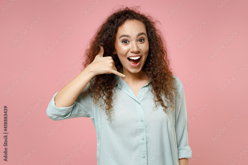 Young black african american friendly cheerful smiling happy positive fun cool curly woman in blue shirt doing phone gesture like says call me back isolated on pastel pink background studio portrait Young black african american friendly cheerful smiling happy positive fun cool curly woman in blue shirt doing phone gesture like says call me back isolated on pastel pink background studio portrait
