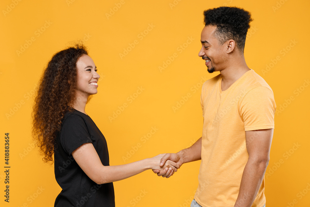 Young couple two friends together family smiling african man woman in black t-shirt hold hands folded handshake gesture friendship business greet concept isolated on yellow background studio portrait. Young couple two friends together family smiling african man woman in black t-shirt hold hands folded handshake gesture friendship business greet concept isolated on yellow background studio portrait.