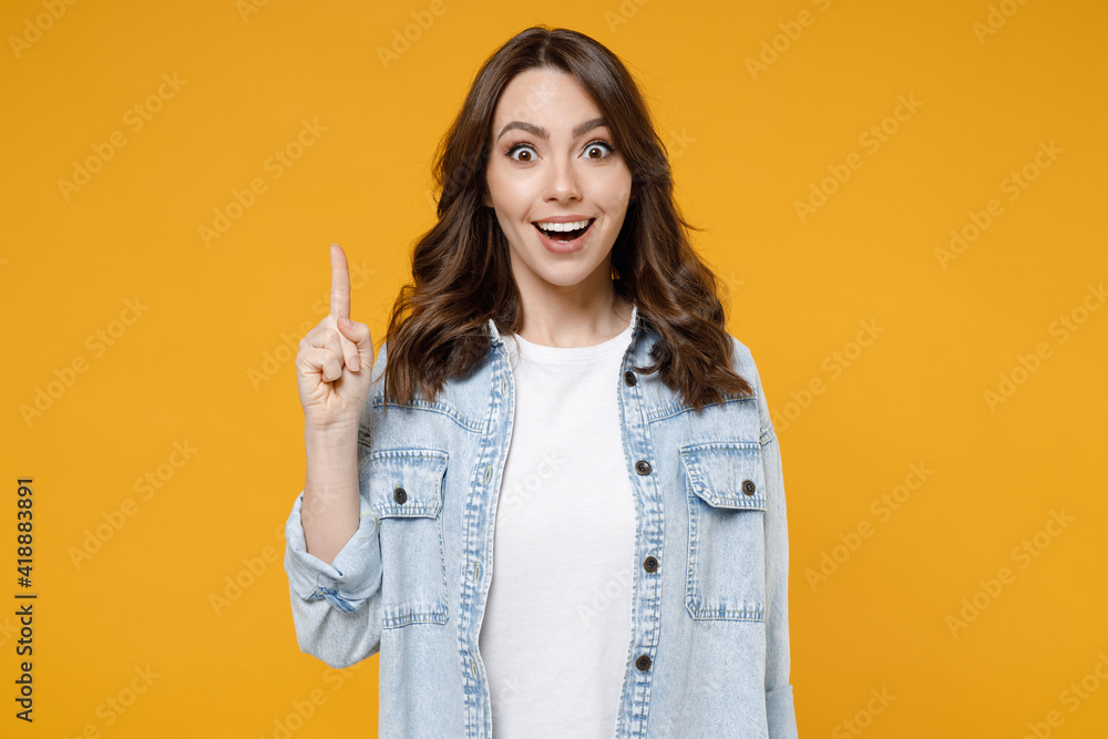 Young caucasian insighted smart proactive excited happy brunette woman 20s in stylish denim shirt white t-shirt hold index finger up with great new idea isolated on yellow background studio portrait. - obrazy, fototapety, plakaty 