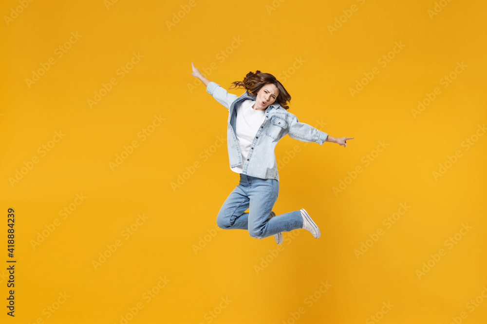 Full length of young overjoyed excited fun expressive student happy woman 20s wear denim shirt white t-shirt with outstretched hands legs jumping high isolated on yellow background studio portrait