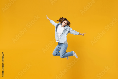 Full length of young overjoyed excited fun expressive student happy woman 20s wear denim shirt white t-shirt with outstretched hands legs jumping high isolated on yellow background studio portrait © ViDi Studio