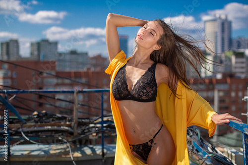 Sexy girl in black underwear and bright yellow summer cape stands on the terrace against the backdrop of the big city. High quality photo