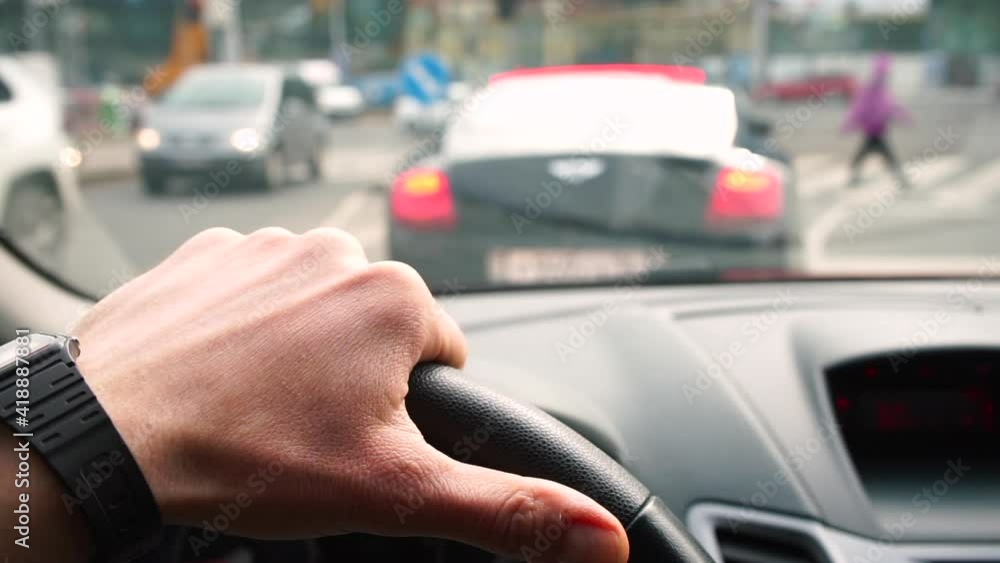 The driver's hand holds the steering wheel of the car. The car is standing, the light is flashing. Waiting time in a traffic jam. The movement of vehicles in the bokeh. The driver's hand holds the steering wheel of the car. The car is standing, the light is flashing. Waiting time in a traffic jam. The movement of vehicles in the bokeh.