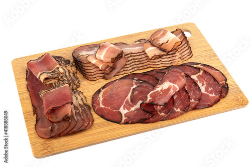Assorted chopped pork brisket, neck and prosciutto on a wooden cutting board. Pork delicacies on a cutting board over white background. Copy space.