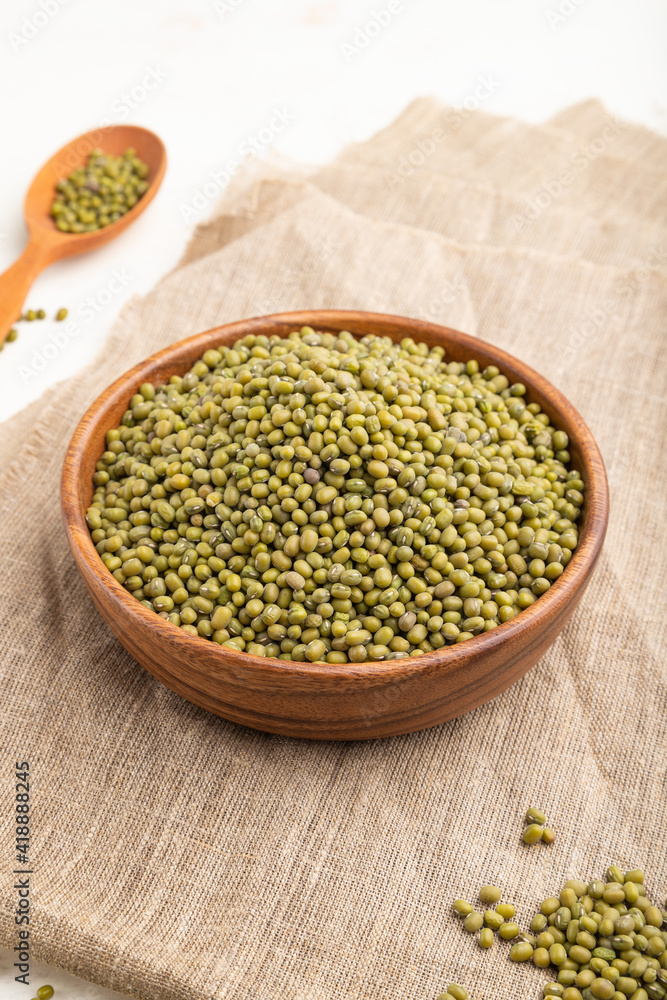 Wooden bowl with raw green mung bean and wooden spoon on a white background. Side view, close up. Wooden bowl with raw green mung bean and wooden spoon on a white background. Side view, close up.
