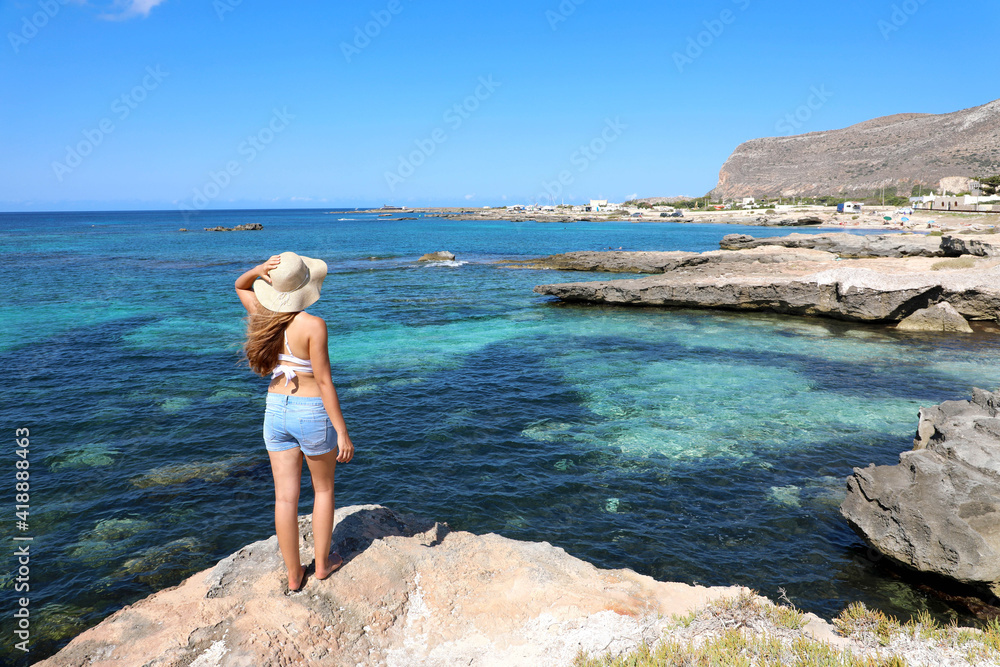 Traveler girl on rocky island landscape with crystalline sea water. Young woman enjoying vacation in Favignana Island, Sicily, Italy.