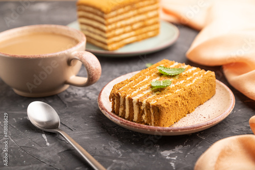 Homemade honey cake with milk cream and mint with cup of coffee on a black concrete background. Side view, selective focus.
