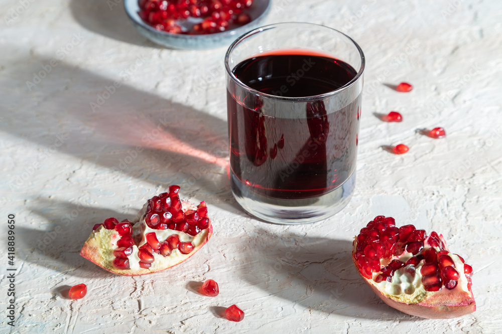 Glass of pomegranate juice on a white concrete background. Hard light, side view. Glass of pomegranate juice on a white concrete background. Hard light, side view.