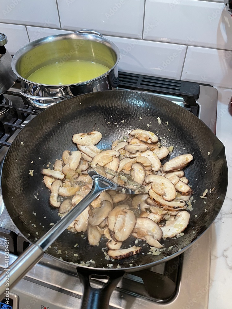 New York. 2021. Chinese meal being cooked using a wok, Chicken stock in a saucepan and mushrooms in a wok to form part of a Chinese meal. New York. 2021. Chinese meal being cooked using a wok, Chicken stock in a saucepan and mushrooms in a wok to form part of a Chinese meal.