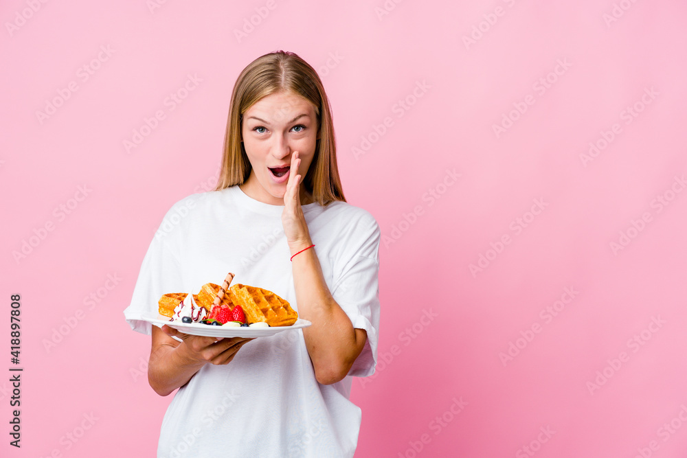 Young russian woman eating a waffle isolated is saying a secret hot braking news and looking aside Young russian woman eating a waffle isolated is saying a secret hot braking news and looking aside