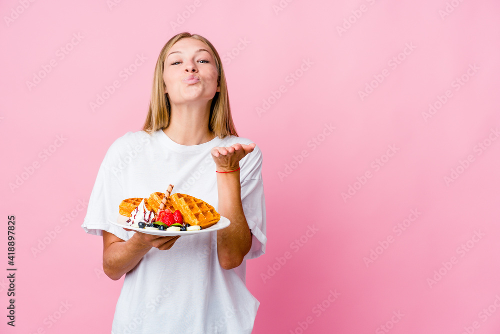 Young russian woman eating a waffle isolated folding lips and holding palms to send air kiss.