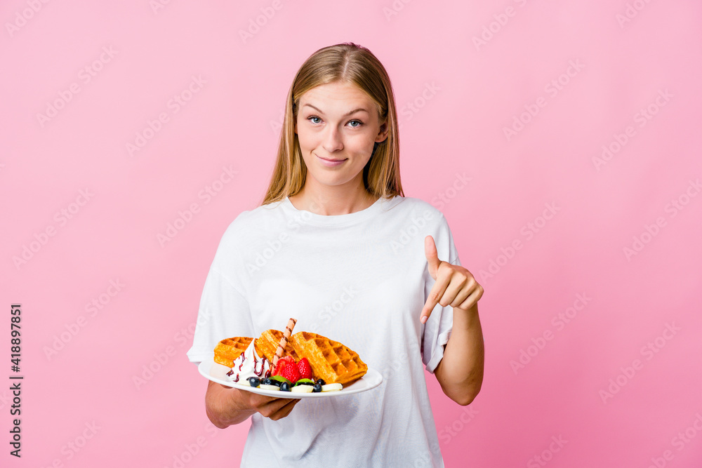 Young russian woman eating a waffle isolated points down with fingers, positive feeling. Young russian woman eating a waffle isolated points down with fingers, positive feeling.
