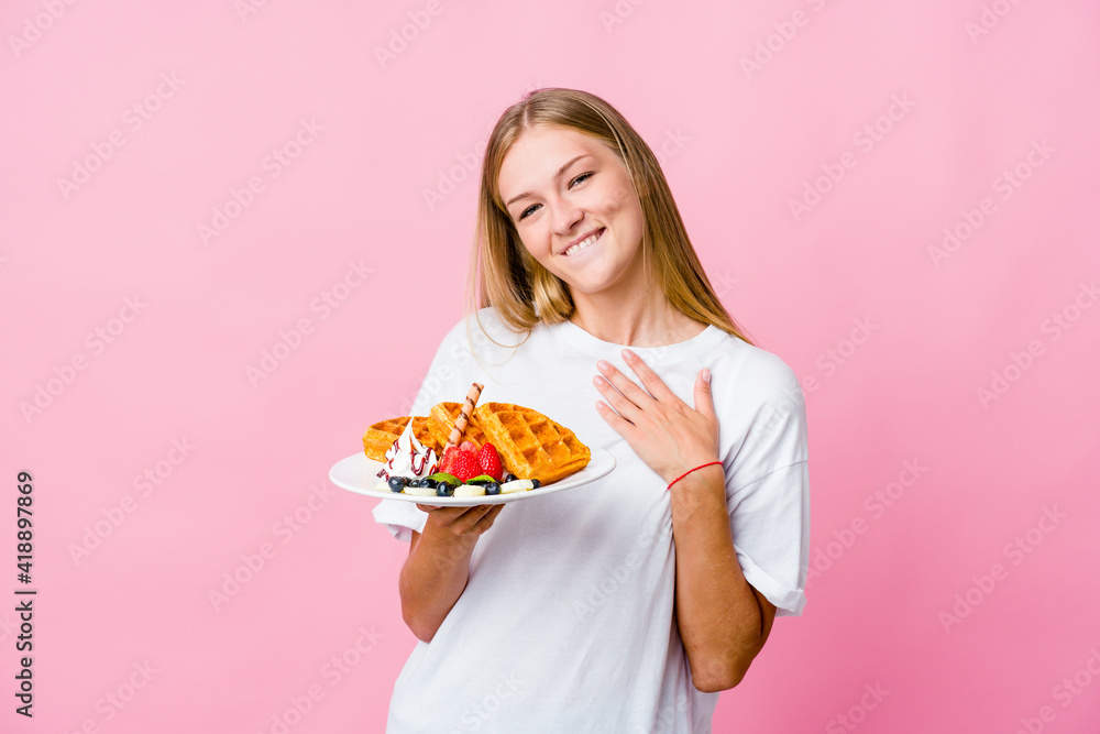 Young russian woman eating a waffle isolated has friendly expression, pressing palm to chest. Love concept. Young russian woman eating a waffle isolated has friendly expression, pressing palm to chest. Love concept.